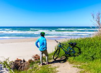 Ustronie Morskie noclegi – rowerzystka na plaży obserwująca morze